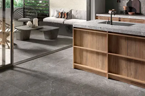 Isola della cucina in legno e zona living sullo sfondo con lo stesso pavimento in gres effetto pietra scura