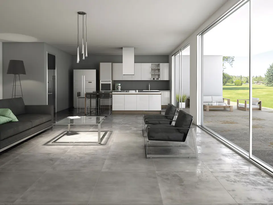 Open space con cucina bianca sul fondo e salotto con poltrone scure, pavimento unico in grandi piastrelle grigie